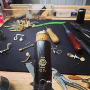 Clarinet barrel with Selmer logo on a workbench surrounded by repair tools.